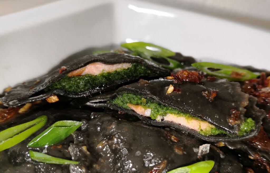 Schwarze Ravioli mit Spinat-Frischkäsecreme und Lachsforelle in Knoblauchbutter mit Röstzwiebeln und Chili